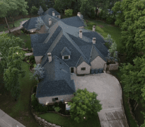 Aerial view of large suburban home with dark roof surrounded by mature trees
