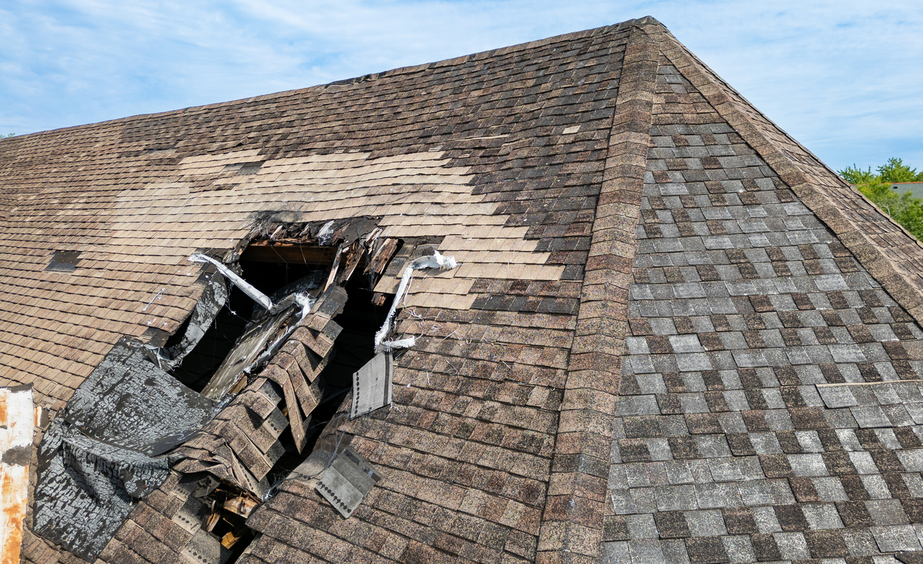 Damaged shingle roof with a large hole and visible damage