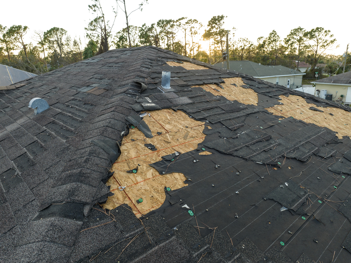 Damaged roof with missing shingles after a storm, trees in background.