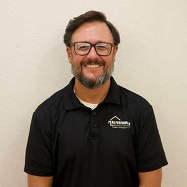 Smiling man in black polo shirt standing against a white background.
