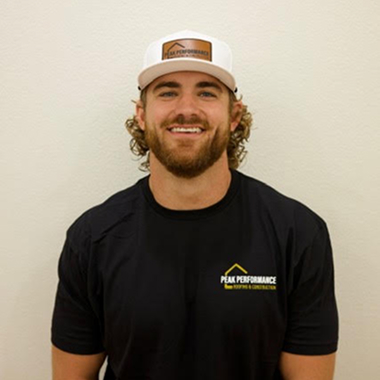 Smiling man wearing 'Peak Performance' shirt and cap.